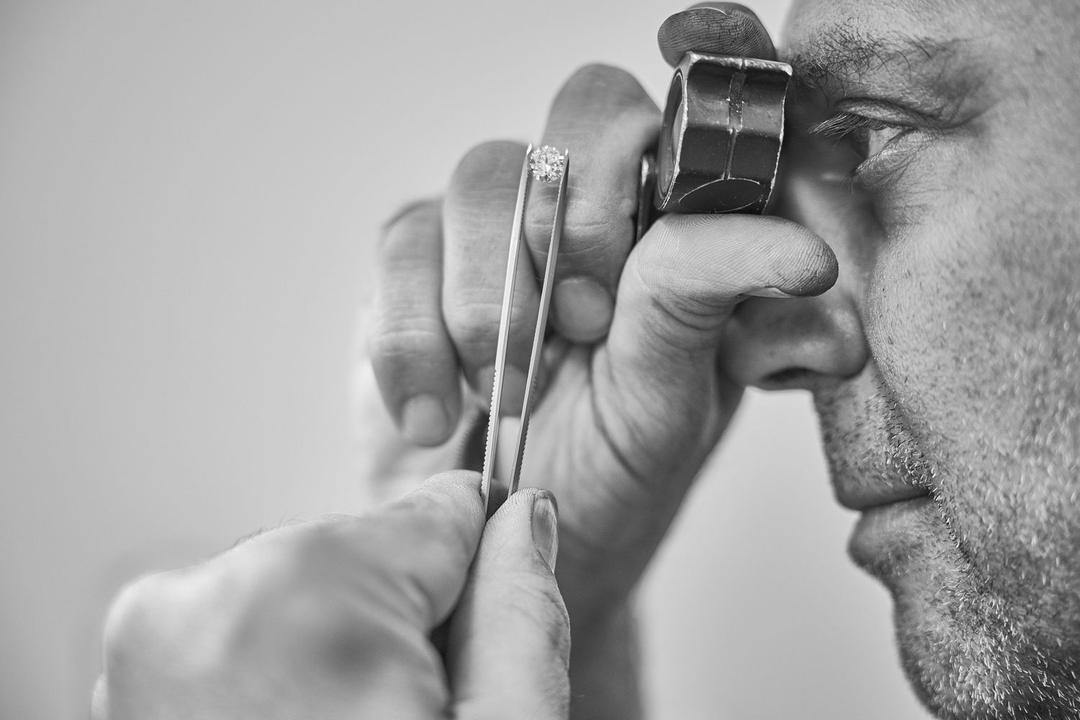 Black and white photograph of a jeweler inspecting a stone through a loupe